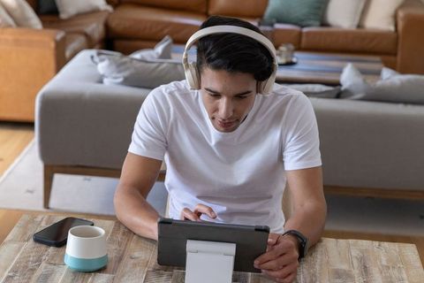 Man wearing headphones using tablet at living room table for remote learning and work