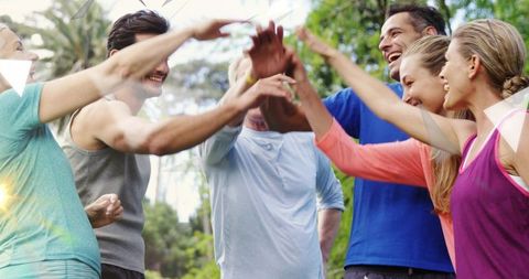 Sunlit group giving high five and cheering after outdoor workout in park — teamwork