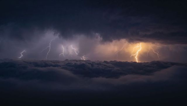 Dramatic lightning cluster striking above dense cloud deck at night with storm illumination