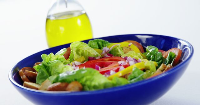This vibrant and colorful fresh garden salad features a variety of vegetables like tomatoes, lettuce, bell peppers, and red onions, served in a striking blue bowl. A bottle of olive oil is placed in the background. Perfect for promoting healthy eating, organic food, salad recipes, and diet plans.