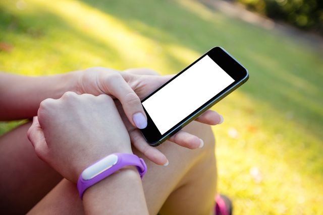 Woman with fitness band on her wrist using her mobile phone in the park