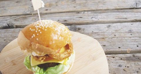 Rustic sesame burger sitting on wooden board at weathered picnic table with copy space