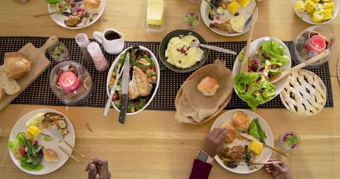 Multiethnic family sharing roasted chicken, salad, pie and bread at communal dining table
