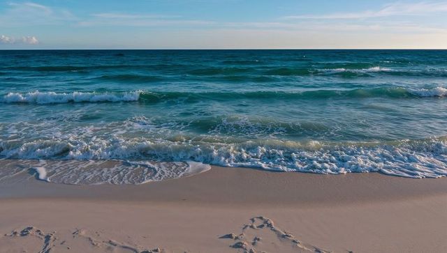 Serene turquoise ocean waves rolling onto pale sandy beach leaving human footprints