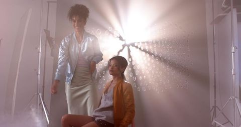 Retro studio fashion duo posing with dramatic backlight, metallic bomber and mustard jacket