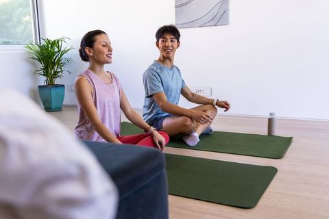 Couple practicing mindful yoga at home with asian man and african american woman