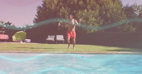 Shirtless man jumping into backyard pool wearing red swim trunks during sunny picnic