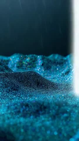 Vertical beam striking shimmering blue teal glitter mounds creating bright particle impact