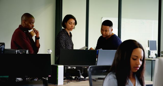 Team members standing and discussing work in a modern open-plan office. Suitable for use in business websites, corporate brochures, and presentations to emphasize teamwork, collaboration, and a productive work environment.