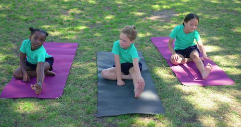 Multicultural girls practicing yoga outdoors on mats in park during sunny day