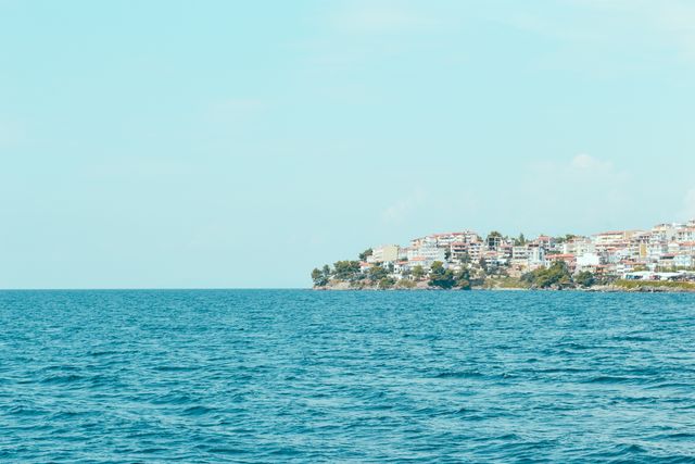 Photo of waterfront homes in a coastal town under a clear blue sky with the tranquil blue sea in the foreground. Ideal for use in travel advertisements, vacation brochures, and websites promoting coastal destinations. Can be used to convey peacefulness, relaxation, and scenic beauty.