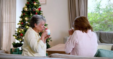 Senior Mother and Daughter Sharing Coffee Near Christmas Tree
