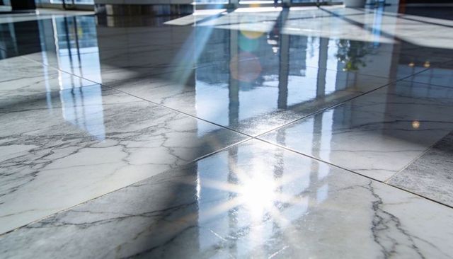 Polished veined marble floor with window reflections and sunlight lens flare in bright atrium lobby