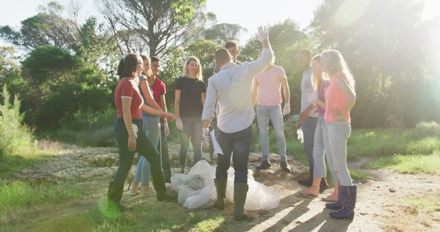 A group of people are collecting litter in a park during the daytime. They are holding garbage bags and standing in a circle, discussing their efforts. The sun is shining, and the background features trees and grass. This can be used for content related to environmental initiatives, community service projects, and volunteer work.