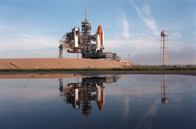 Space Shuttle Atlantis is seen at Launch Pad 39A with its rotating service structure rolled back, reflecting in water. This marks the preparations for Mission STS-86, set to launch three weeks later. This mission will involve docking with the Russian Space Shuttle Mir and the transfer of science equipment and an astronaut. Ideal for articles and educational materials on space exploration, NASA missions, and international space cooperation.