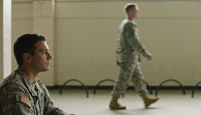 Contemplative u.s. Army soldier sitting and watching indoor training hall with flag patch