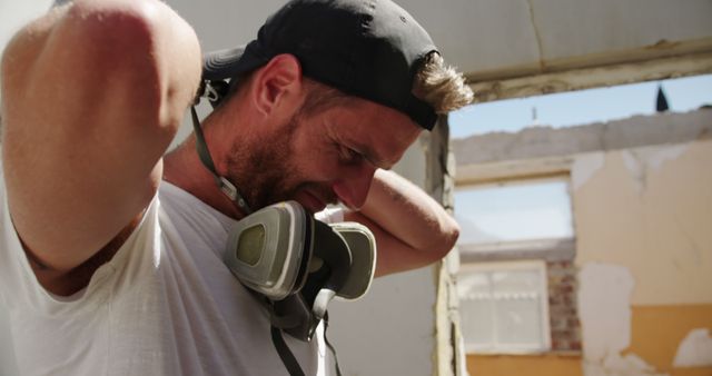 Construction worker with respirator adjusting cap during renovation work - Download Free Stock Images Pikwizard.com