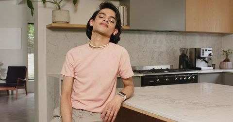 Asian man leaning on marble kitchen island wearing pearl necklace and smartwatch