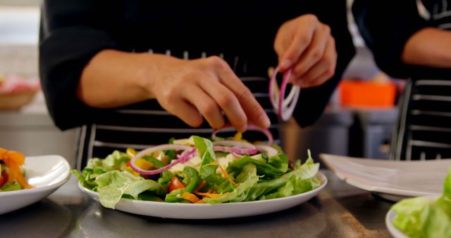 A chef is garnishing a colorful salad with red onion slices, with copy space. The image captures the final touches being added to a fresh dish, emphasizing the importance of presentation in culinary arts.