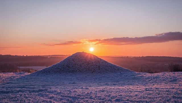 Snow-covered mound backlit by golden sunset over frosty meadow at twilight