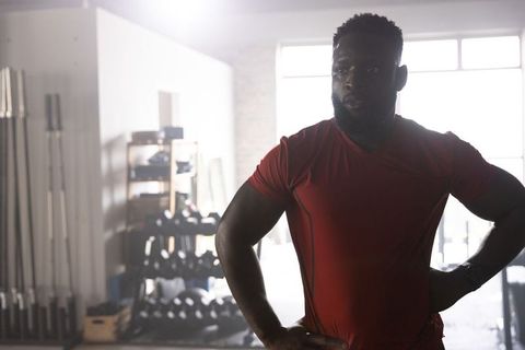 Backlit african american athlete standing hands-on-hips in industrial gym with dumbbells