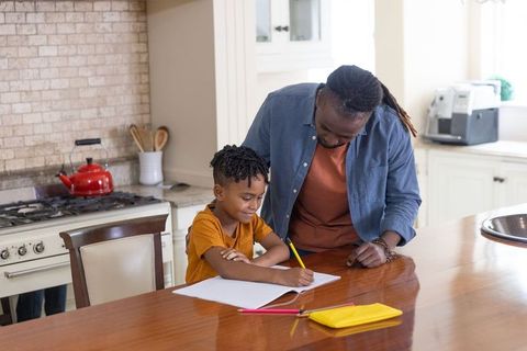 African american father helping son with homework at bright kitchen island