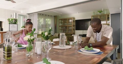 African American father and daughter arranging dining table for family celebration in sunlit home