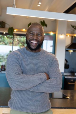 Confident smiling african american man standing in open-concept kitchen wearing grey sweater