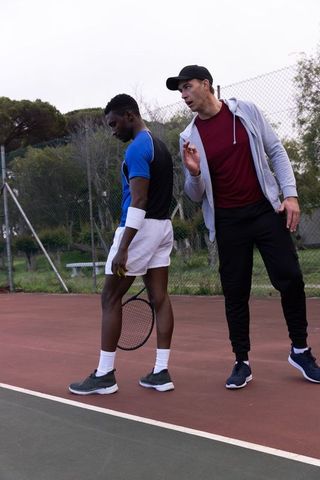 White coach instructing black player practicing tennis outdoor hardcourt courtside training