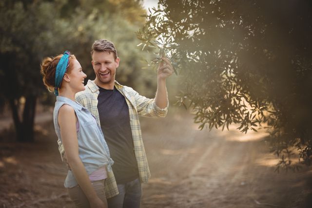 Cheerful young couple standing by olive tree at farm