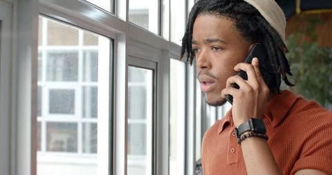 African American Man Standing by Window Making Phone Call and Looking Out Thoughtfully