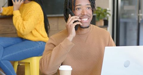 Smiling young professional talking on phone while working on laptop in modern cafe