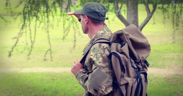 A middle-aged Caucasian man in military attire is hiking with a large backpack, with copy space. His journey through a green landscape suggests a training exercise or a personal adventure in nature.