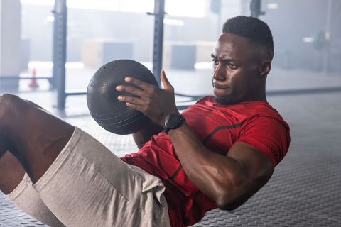 African american man performing medicine ball russian twist in gym for core strength