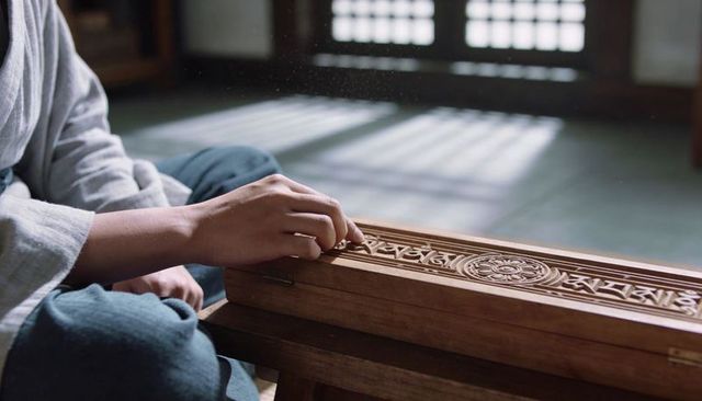 Hand plucking carved wooden zither guqin in traditional room with soft lattice light