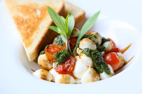 Serving caprese salad with mozzarella pearls, cherry tomatoes and basil pesto with toasted bread