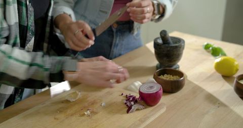 Two women chopping red onion on wooden countertop with mortar and pestle, citrus, teamwork