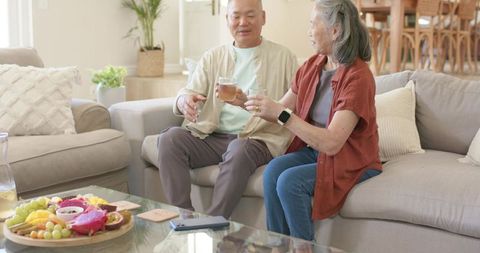 Senior asian couple sharing tea and conversation on cozy sunlit living room sofa