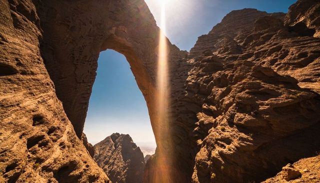 Sunbeam framing natural rock arch revealing jagged peaks in arid desert canyon