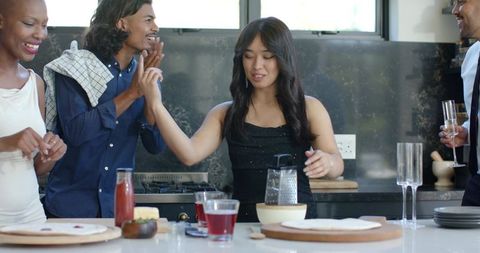 Diverse friends celebrating at kitchen island grating cheese and toasting with champagne