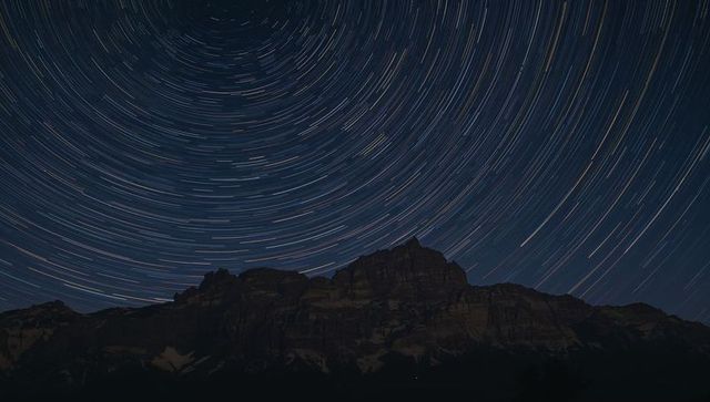 Circling Star Trails Over Jagged Alpine Ridge at Night with Snow Patches and Treeline Silhouette