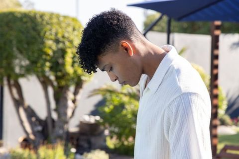 African american young man standing in sunny backyard looking down wearing white shirt