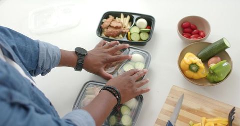African man placing lids on meal prep containers on white countertop with fresh vegetables