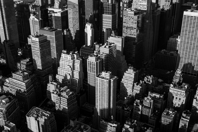 This aerial perspective of a city features numerous towering skyscrapers and commercial buildings, providing a classic black and white view of a bustling metropolis. Ideal for use in articles or projects about urban development, real estate, architecture, or city planning. The monochromatic aesthetic adds a timeless and sophisticated element fitting for editorial purposes or background imagery.