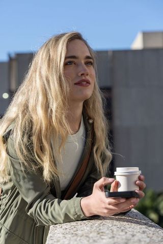 Young woman enjoying coffee checking phone on urban rooftop terrace under clear sky
