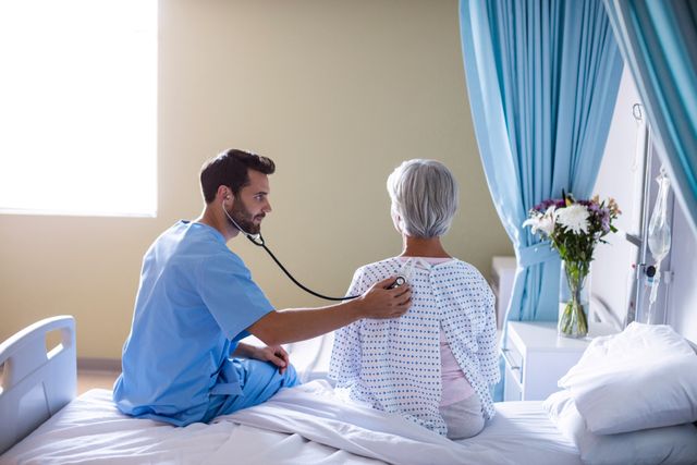 Male doctor examining senior female patient with stethoscope in hospital room. Ideal for use in healthcare, medical, and senior care related content. Can be used in articles, brochures, and websites focusing on patient care, medical services, and elderly health.
