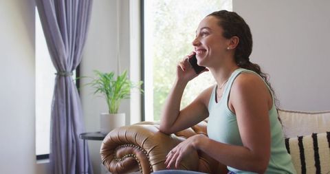 Woman Relaxing on Couch and Talking on Smartphone by Window