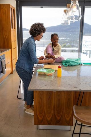 Mother packing lunch with daughter in modern kitchen interior
