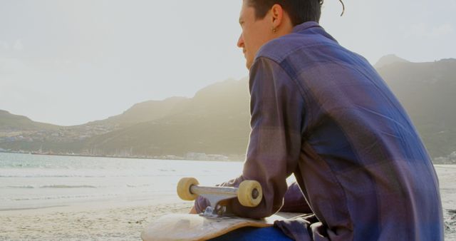 Young Man with Skateboard Sitting on Beach at Sunset - Download Free Stock Images Pikwizard.com