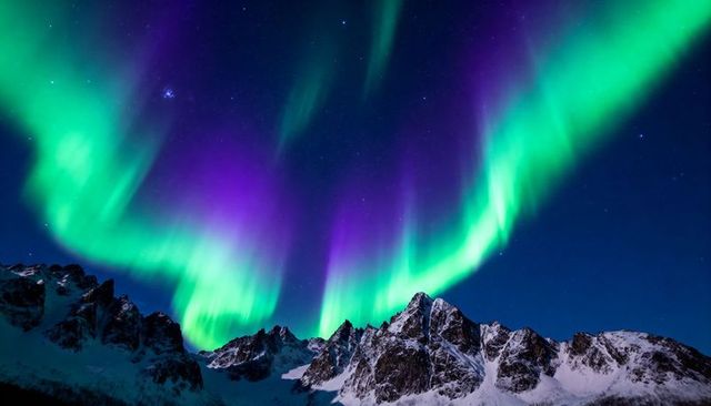 Vivid green aurora curtains dancing over jagged snowy peaks under starry polar night sky